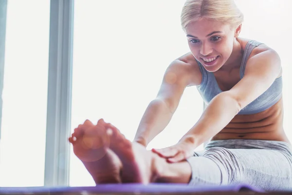 Beautiful young woman in sports wear is smiling while stretching on a yoga mat