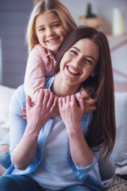 Güzel genç anne ve kızını sarılma, evde kanepede otururken gülümseyen ve kameraya bakarak portre