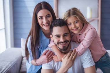 Güzel genç anne, baba ve sarılma, evde kanepede otururken gülümseyen ve kameraya bakarak onların kız portresi