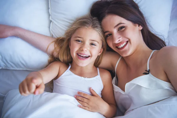 美しい若い母と娘を抱いて カメラ目線し ながら自宅のベッドで横になっている笑顔の平面図 — ストック写真