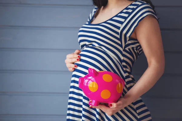 貯金箱を押しながら腹 灰色の壁に立っている つの手を保つ美しい妊娠中の女性の画像をトリミング — ストック写真