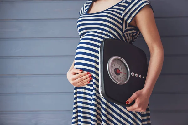 美しい妊婦腹 灰色の壁に立っている体重計と維持する つの手を保持してのトリミングされた画像 — ストック写真