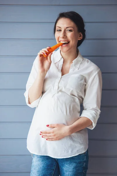 Piękna Kobieta Ciąży Jest Jedzenie Marchew Trzymając Jedną Ręką Brzuch — Zdjęcie stockowe