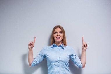 Klasik giysiler içinde Çekici kız işaret ederken gülümsüyor ve yukarı bakıyor, gri arka plan karşı