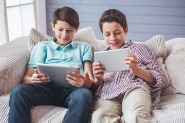 İki çekici genç çocuklar tablet kullanarak ve evde kanepede otururken gülümseyen
