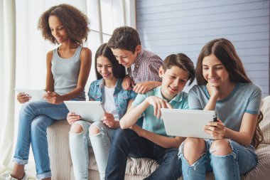Genç erkek ve kız grup tablet kullanarak, söz ve evde kanepede otururken gülümseyen