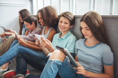 Genç erkek ve kız grup tablet kullanarak ve yerde otururken gülümseyerek. Bir çocuk kameraya bakıyor