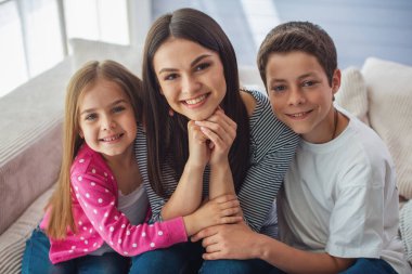 Güzel genç anne, onun sevimli küçük kızı ve oğlu kamera bakıyor ve gülümsüyor, evde kanepede oturuyor