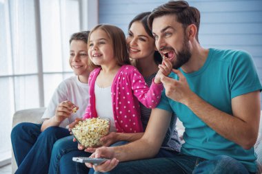 Güzel genç anne- babalar, kızları ve oğulları tv izliyorlar, patlamış mısır yiyor ve gülümsüyor, evde kanepede oturuyorlar. Babam uzaktan kumanda kullanıyor.