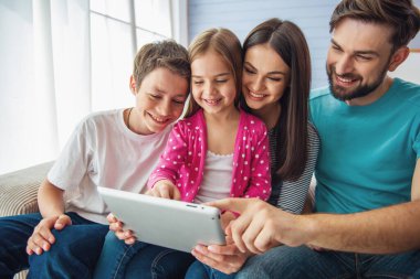 Güzel genç anne, onların sevimli küçük kızı ve oğlu evde kanepede oturan, bir tablet kullanıyor ve gülümseyerek