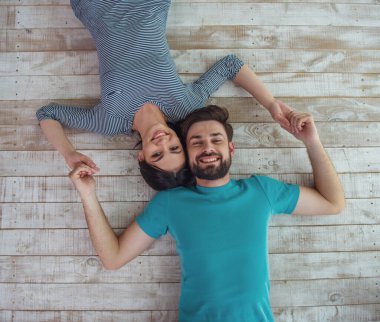 Güzel genç kadın ve el ele tutuşarak, kameraya bakıyor ve gülümsüyor, ahşap yerde yatarken yakışıklı delikanlı Üstten Görünüm