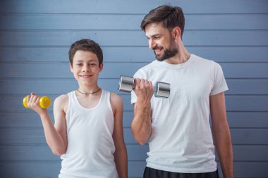 Yakışıklı genç Baba ve onun genç oğlu kameraya bakarak ve dumbbells ile dışarı çalışırken gülümseyen