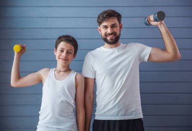 Yakışıklı genç Baba ve onun genç oğlu kameraya bakarak ve dumbbells ile dışarı çalışırken gülümseyen