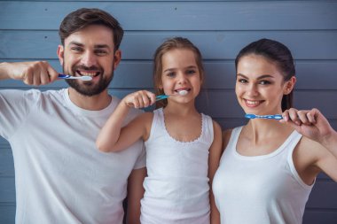 Güzel anne ve sevimli küçük kızları kameraya bakarak ve gri duvara diş fırçalama sırasında gülümseyen