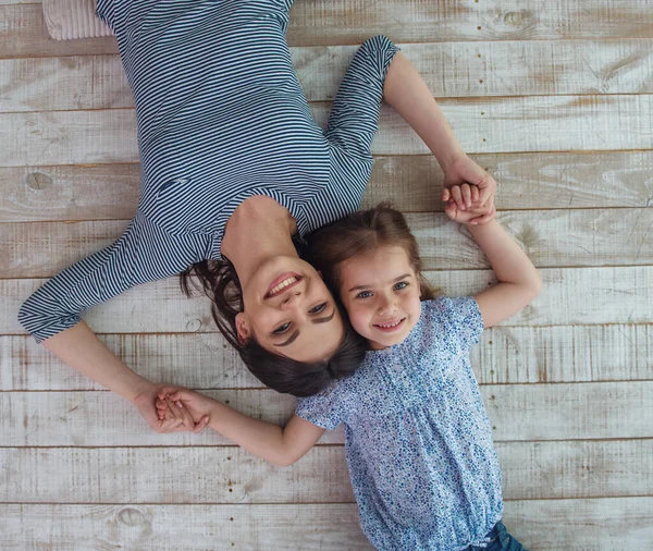 美しい若い母親と彼女のかわいい小さな娘が手をつないで カメラを見て 笑顔で 木製の床に横たわっているトップビュー — ストック写真