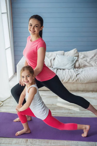 漂亮的年轻妈妈和她可爱的小女儿看着相机 微笑着拉伸对瑜伽垫在家里 — 图库照片