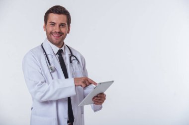 Yakışıklı doktor beyaz paltolu bir tablet kameraya bakıyor ve gülümsüyor, izole üzerinde beyaz arka plan kullanıyor