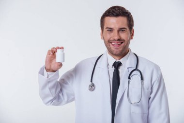 Kameraya bakıyor ve gülümsüyor, izole üzerinde beyaz arka plan beyaz paltolu yakışıklı doktor ilaç, bir şişe tutuyor