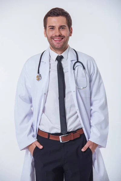 穿白大褂的帅医生看着相机和微笑着用手在口袋里 站在白色背景上孤立 — 图库照片