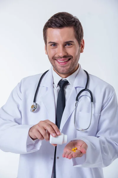 白衣でハンサムな医者は薬の瓶を持って 彼の手のひらに薬を追加する カメラ目線 笑みを浮かべて 上分離ホワイト バック グラウンド — ストック写真
