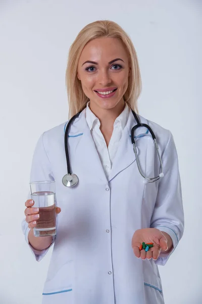 白いコートを着た美しい女性医師の肖像画は 水と錠剤のグラスを持ち カメラを見て 笑顔で 白い背景に隔離された — ストック写真