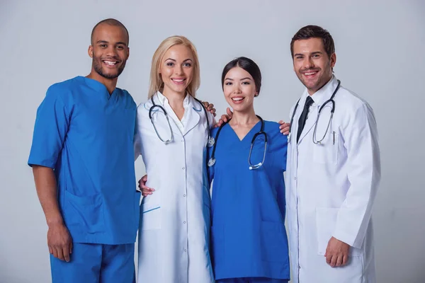 Group of medical doctors of different nationalities and genders is looking at camera and smiling, standing on gray background