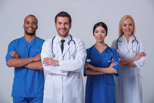 Group of medical doctors of different nationalities and genders is looking at camera and smiling, standing with crossed arms on gray background