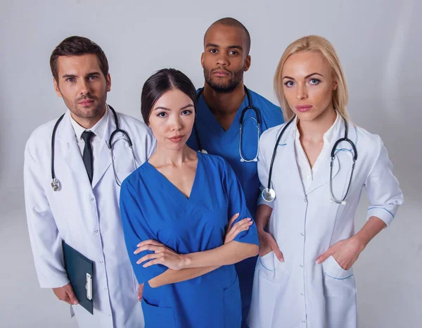 Group of medical doctors of different nationalities and genders is looking at camera, standing on gray background