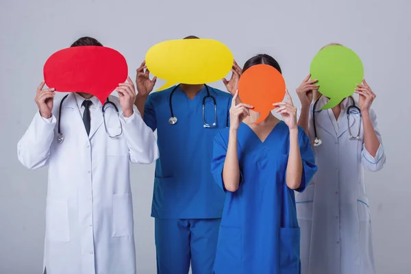 Group of medical doctors of different nationalities and genders is covering faces with speech bubbles, standing on gray background