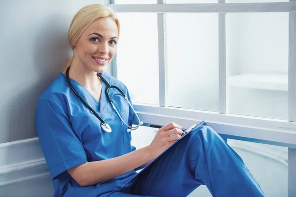 Piękna Blondynka Lekarka Niebieski Nosić Medycznych Jest Dokonywanie Notatek Patrząc — Zdjęcie stockowe