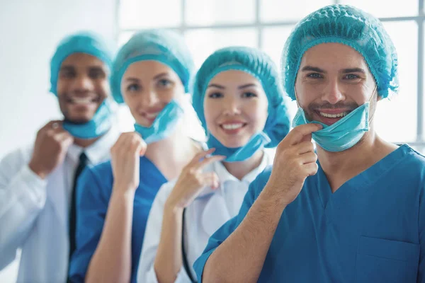 Lekarze Różnych Narodowości Płci Czapki Ciągnąc Maski Patrząc Kamery Uśmiechnięty — Zdjęcie stockowe