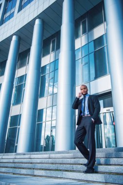Klasik takım elbiseli, cep telefonuyla konuşan, ofis binasının merdivenlerinde duran yakışıklı genç iş adamının tam boy portresi.