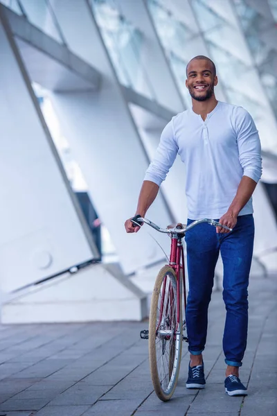 自転車で屋外に歩いている間 カジュアルな服のハンサムな若いビジネスマンが笑っています — ストック写真