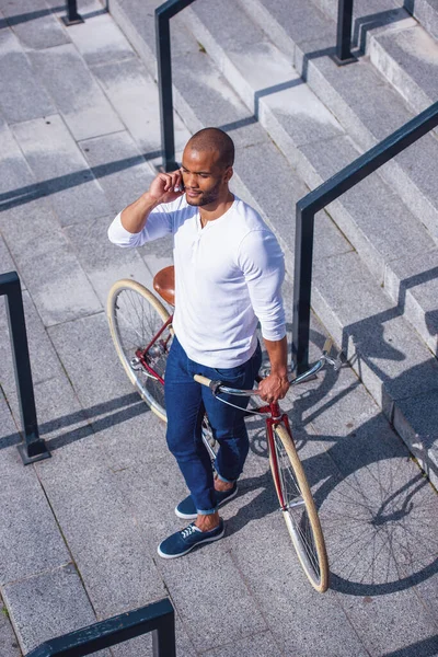 年轻英俊的商人穿着休闲装 戴着手机 骑着自行车站在外面的楼梯上 高瞻远瞩 — 图库照片