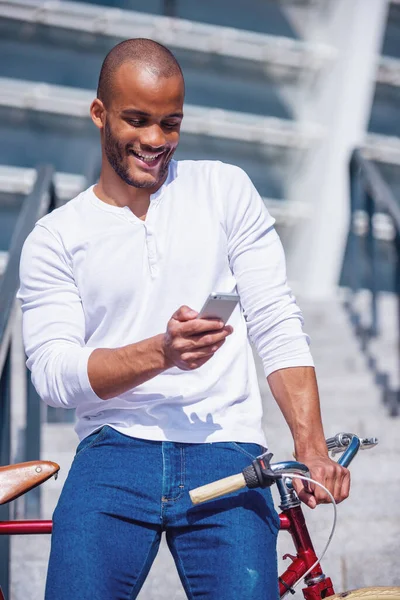 穿着休闲装的年轻貌美的商人一边骑自行车一边用智能手机和微笑 站在户外 — 图库照片