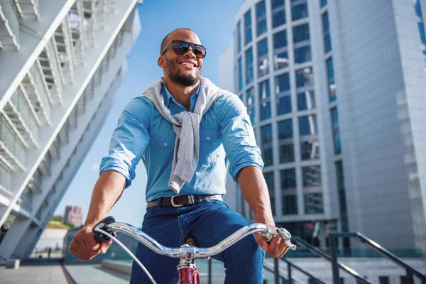 彼の自転車に乗ってカジュアルな服やサングラスでハンサムな若いビジネスマンの低角度ビューと笑顔 — ストック写真