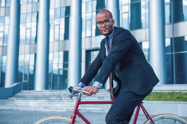 オフィスビルの外で自転車に乗っている間 古典的なスーツと眼鏡でハンサムなビジネスマンの側面図 — ストック写真