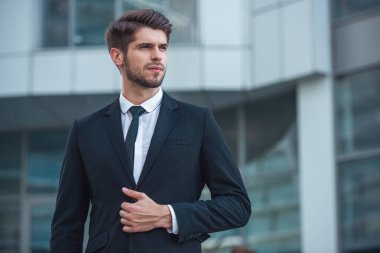 Yakışıklı genç emin işadamı Klasik takım elbiseli, ofis binası dışında ayakta arıyor