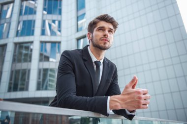 Yakışıklı genç emin işadamı Klasik takım elbiseli, balkon korkuluk ofis binası dışında üzerine eğilerek arıyor