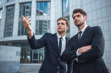 Klasik takım elbiseli iki yakışıklı genç işadamları arıyor ve uzağa işaret, ofis binası dışında duran
