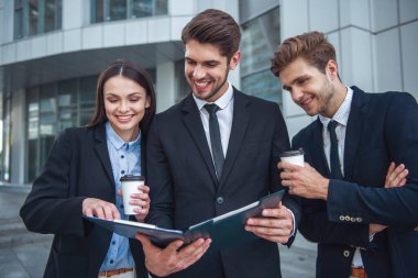 İki yakışıklı genç işadamları ve Bayan kahve ile bir klasör holding, belgeleri inceleyerek ve gülümseyen, ofis binası dışında duran