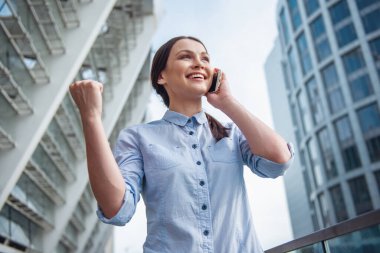 Mobil telefonda konuşurken ve gülümseyen, ofis binası dışında Balkonda duran güzel genç iş kadını düşük açılı görünümü