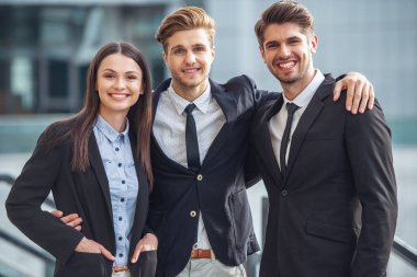 İki yakışıklı genç işadamları ve klasik giyim Bayan kameraya bakıyor ve gülümsüyor, açık havada duran