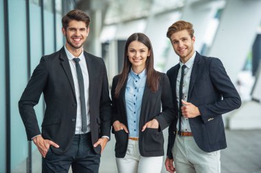 İki yakışıklı genç işadamları ve klasik giyim Bayan kameraya bakıyor ve gülümsüyor, ayakta, elleri ceplerinde, ofis binası yakınındaki