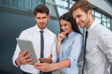 İki yakışıklı genç işadamları ve klasik giyim Bayan tablet kullanma ve gülümseyen, office ayakta