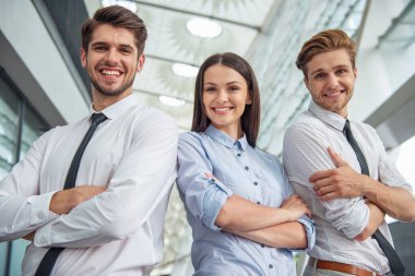 İki yakışıklı genç işadamları ve klasik giyim Bayan kameraya bakıyor ve gülümsüyor, ofis binası yakınındaki çapraz kollar ile ayakta