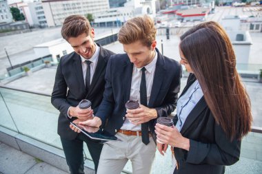 İki yakışıklı genç işadamları ve klasik giyim Bayan tablet kullanma, bardak kahve holding ve gülümseyen, ofis binası Balkonda duran