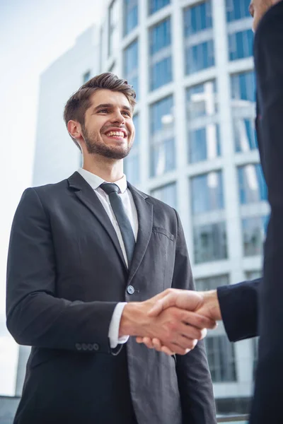 彼の同僚と握手と笑顔 オフィスビルの外に立って古典的なスーツでハンサムな青年実業家のローアングル ビュー — ストック写真