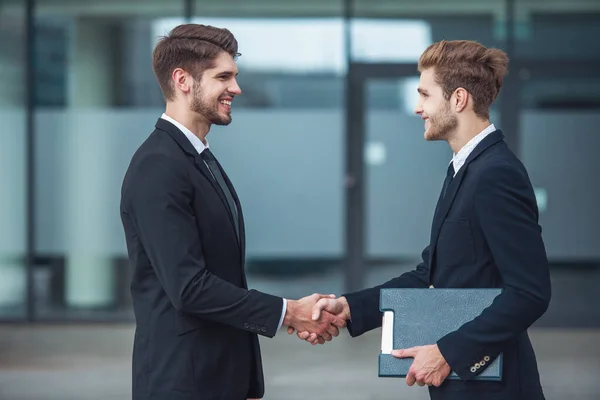 古典的なスーツ姿の 人のハンサムな若いビジネスマンに手を振って お互いを見て 笑みを浮かべて オフィスビルの外に立って — ストック写真