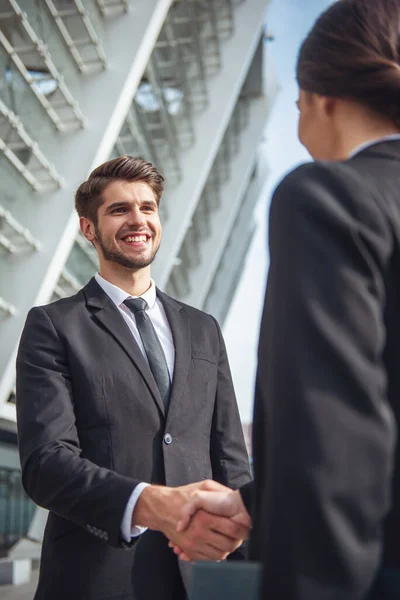 古典的なスーツでハンサムな青年実業家の彼の同僚と握手し笑顔 オフィスビルの外に立って — ストック写真
